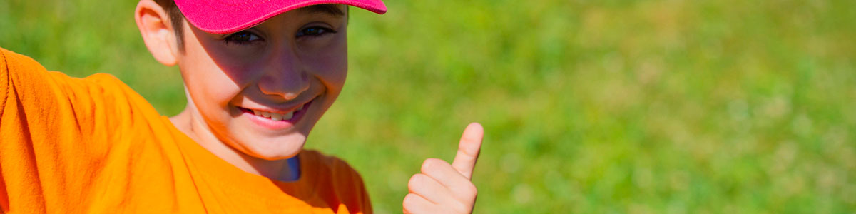 Little boy smiling giving thumbs up on a lawn